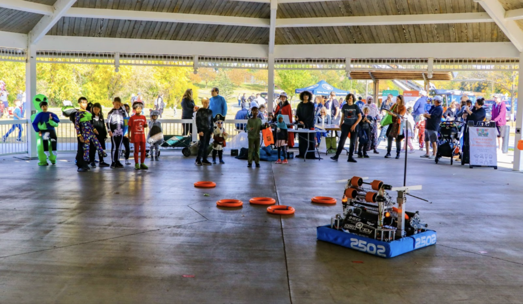 People surrounding Cronus (robot) and throwing rings